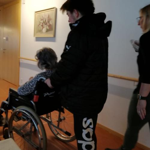 Schüler führt eine Dame im Rollstuhl