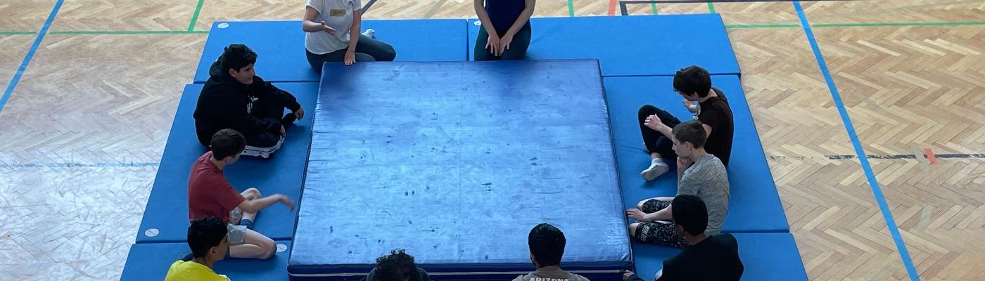 Schüler sitzen um den Weichboden herum. 